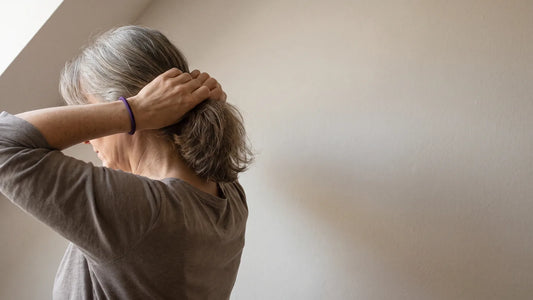 Frau um die fünfzig fasst ihr feines Haar im Nacken zusammen, als Sinnbild für Haarausfall bei Frauen und dessen Ursachen